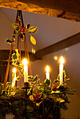 Detail of candle lit chandelier decorated with holly and spruce hanging from a beam