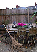 Tisch und Stühle im Freien in einem umzäunten Garten mit Laternen und rosa Blumen