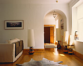 Lamps with oversized shades stand on glass plinths in living room with rug and arched Palladian doorway