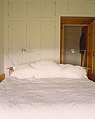 Bett mit weißer Bettwäsche und Winkellampen Einbauschränke und offene Tür