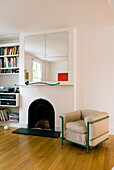 Mirror above fireplace in white living room with armchair and shelving