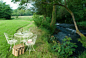 Table and chairs on riverbank with selection of wine in a basket