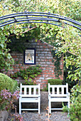 Gartenstühle an einer Backsteinmauer unter einer Laube