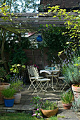 Patio area in back garden with white ornamental metal garden furniture and blue glass lantern hanging from rustic arbour