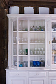 Weiß gestrichene Kommode mit offenen Türen, die eine Sammlung von Glaswaren auf Regalen präsentiert
