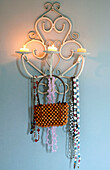 Perlentasche und Halsketten hängen an einem an der Wand befestigten Kerzenhalter