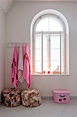 Pink towels above floral pouf at arched window of Odense bathroom