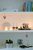 Christmas ornaments and eucalyptus with a crocuses and lit candles on shelving 