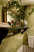 Cut flowers on wall shelf with salvaged mirror and branch of climbing rose