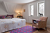 Gefaltete Decke auf gepolstertem Stuhl mit bunt gemustertem Teppich in modernem Schlafzimmer in Odense Dänemark
