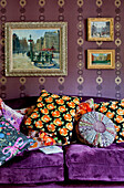 Assorted and brightly coloured cushions on purple sofa under artwork in London home UK