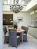 Ornate chandelier hangs above wooden dining table with wicker chairs in West London townhouse conservatory extension England UK