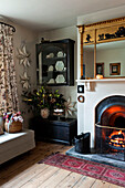 Lit fire and wall mounted display cabinet in Walberton home, West Sussex, England, UK