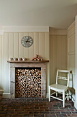 Stuhl neben einem Kamin voller Holzscheite in einem Haus in Buckinghamshire, England, UK