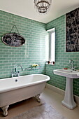 Stehendes Waschbecken und freistehende Badewanne im grün gefliesten Badezimmer eines Einfamilienhauses in Bovey Tracey, Devon, England