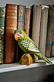 Bemalter Papagei und gebundene Bücher auf einem Regal in einem Bauernhaus in Suffolk, England, Vereinigtes Königreich