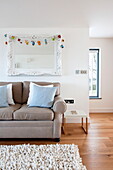 Zweisitzer-Sofa unter verschnörkeltem weißen Spiegel im Wohnzimmer eines Hauses in Wadebridge, Cornwall, England, UK