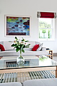 Lilies on glass coffee table with sofa and artwork in contemporary home, Cornwall, England, UK