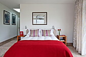Red woollen blanket on double bed with striped pillows in contemporary home, Cornwall, England, UK