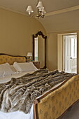 Double bed with fur throw and wooden framed mirror in contemporary Suffolk country house, England, UK