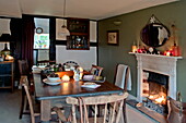 Wooden dining table and chairs with lit fire in Shropshire cottage, England, UK