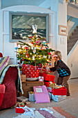 Kleiner Junge betrachtet Geschenke unter dem Weihnachtsbaum in Penzance in Cornwall, England
