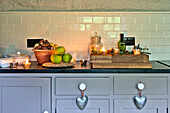 Beleuchtete Teelichter mit Äpfeln und Nüssen auf grauer Küchenarbeitsplatte mit silbernen Herzen in einem Haus in Tregaron, Wales, UK