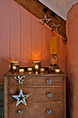 Holzkommode mit sternförmigen Dekorationen und Kerzenhaltern im pfirsichfarbenen Schlafzimmer eines Hauses in Tregaron, Wales, UK