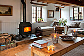 Befeuerter Holzofen mit Teelichtern auf dem Couchtisch im Wohnzimmer einer umgebauten Scheune in Sherford, Devon, Großbritannien