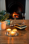 Lit candles with cut thistles on table at fire with glowing embers of fire in Crantock home Cornwall England UK