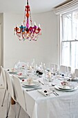 Beaded chandelier hangs above white dining table for eight in Penzance family home Cornwall England UK