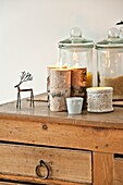Storage jars and lit candles with metal reindeer on wooden sideboard in Wadebridge home, North Cornwall, UK