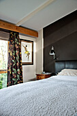 White bedspread with floral curtains at window of Cornwall home, UK