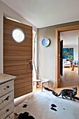 Cream chest of drawers and wooden door with porthole window in Cornwall entrance hallway UK