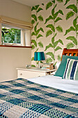 Karierte Decke auf einem Doppelbett in einem Zimmer mit blattgemusterter Tapete in einem Haus in Cornwall England