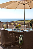 Wicker chairs at table with parasol on terrace, Cornwall, UK