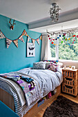 Wimpel an blauer Wand über Einzelbett mit gestreifter Bettdecke am Fenster eines Kinderzimmers in East Grinstead, West Sussex, England UK