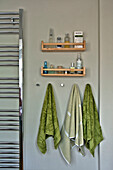 Green hand towels below wooden shelves with wall-mounted radiator in East Grinstead family home West Sussex England UK