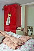 Red painted wardrobe in bedroom with floral quilts in Cambridge cottage England UK