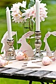 Easter rabbits and silver candlesticks with cut flowers on Sussex garden table England UK