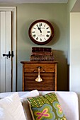 Clock above vintage wooden cabinet and sofa with cushion in Edworth living room Bedfordshire England UK