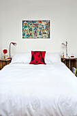 Kunstwerk über einem Doppelbett mit Seitenlampen und Kissen mit religiösem Symbol im Schlafzimmer eines Stadthauses in Cornwall England UK