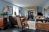 Upholstered armchair with exposed stone fireplace in living room of holiday cottage Cornwall UK