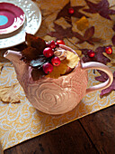 Berries and leaves in white ceramic teapot on wooden dining table in UK home