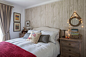 Circular mirror with fairylights above chest of drawers at bedside in Penzance farmhouse Cornwall UK