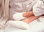 Frau entspannt sich in weißen Filzpantoffeln mit hochgelegten Füßen auf einem bequemen Sofa