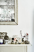Ein schlanker Kaminsims in der Küche, auf dem Feen und kleine Gegenstände ausgestellt sind, mit einem französischen Spiegel mit Stockflecken