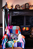 Weihnachtsgirlanden auf dem Kaminsims über einem Sessel mit Strickdecke am beleuchteten Kamin in einem Landhaus in Shropshire, England, UK