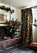 Evergreens and holly berries on antique wooden bench with heavy curtains in Shropshire cottage England UK