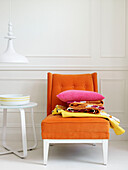 Verschiedene Stoffe und rosa Kissen auf orangefarbenem Stuhl